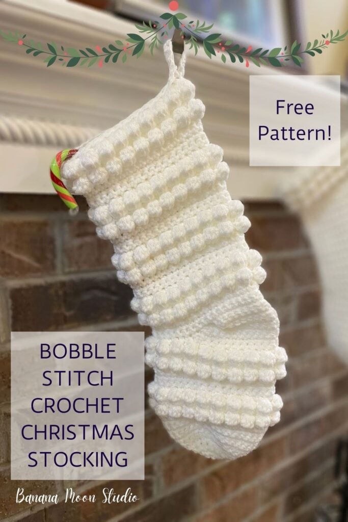 White crochet Christmas stocking hanging from a white mantle piece and brick fireplace. Text reads: Free pattern! Bobble stitch crochet Christmas stocking. Banana Moon Studio.