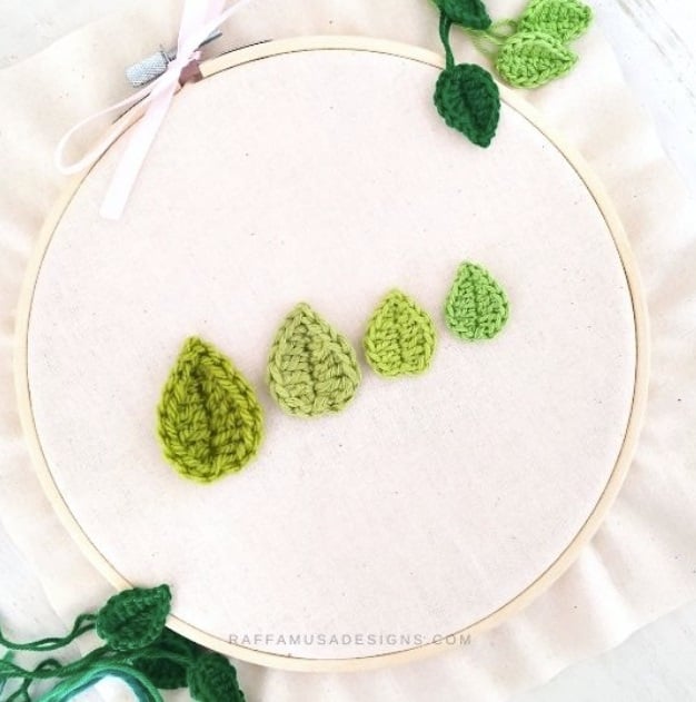 Four sizes of crochet leaves, each a different shade of green, lined up on a peace of muslin set in an embroidery hoop. Additional crochet leaves garnish the edges. Text on the image reads: raffamusadesigns.com.