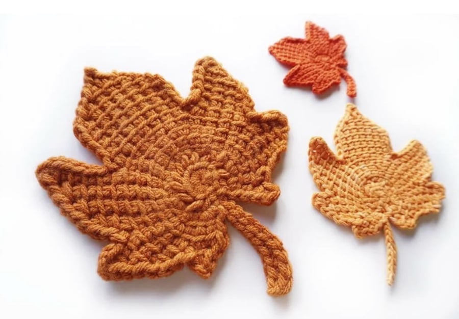 Three orange Tunisian crochet leaves sitting together on a white surface.