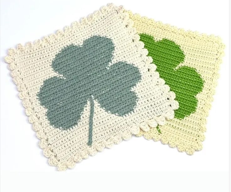 Two crochet washcloths in slightly different colors, each featuring a green shamrock worked in intarsia.