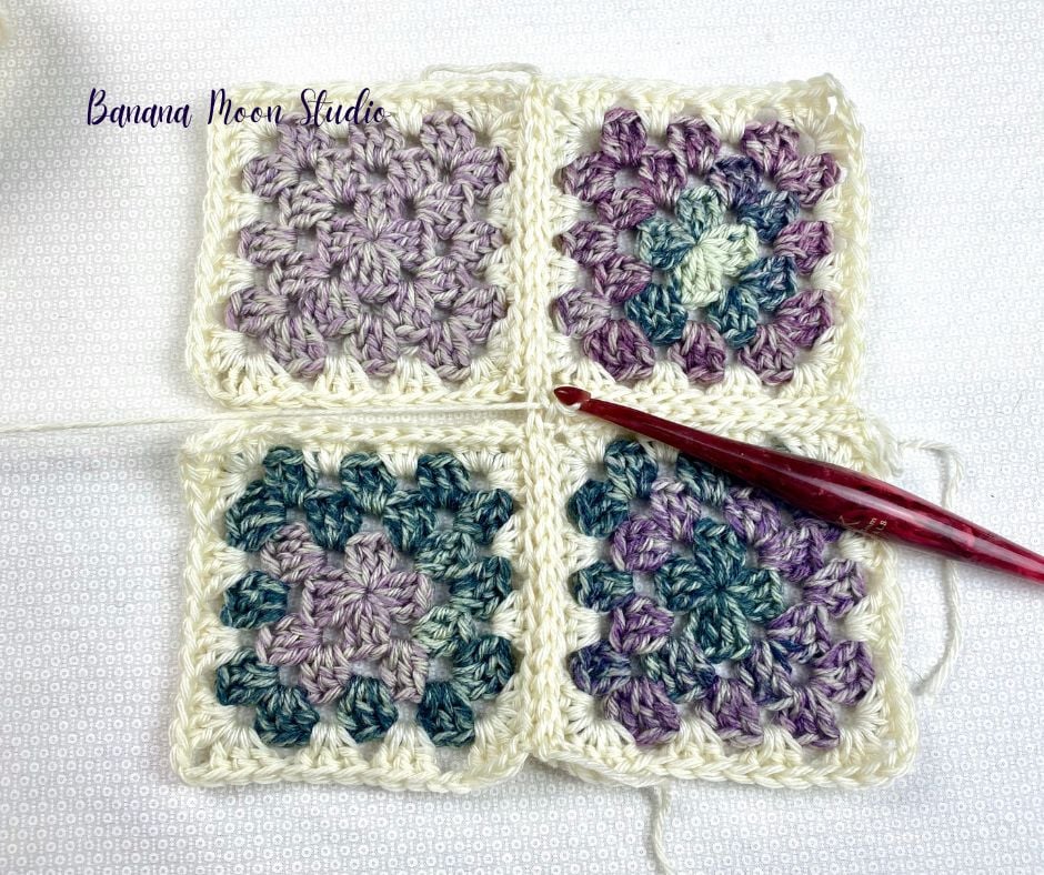 Four crochet granny squares on a white surface with a red crochet hook. The crochet hook is in the process of joining the squares together. Text on the image reads: Banana Moon Studio.