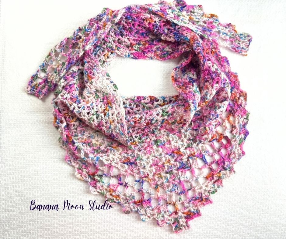 Crochet triangular scarf laying flat on a white surface and wrapped into a circle as if it were being worn. Text on the image reads: Banana Moon Studio.
