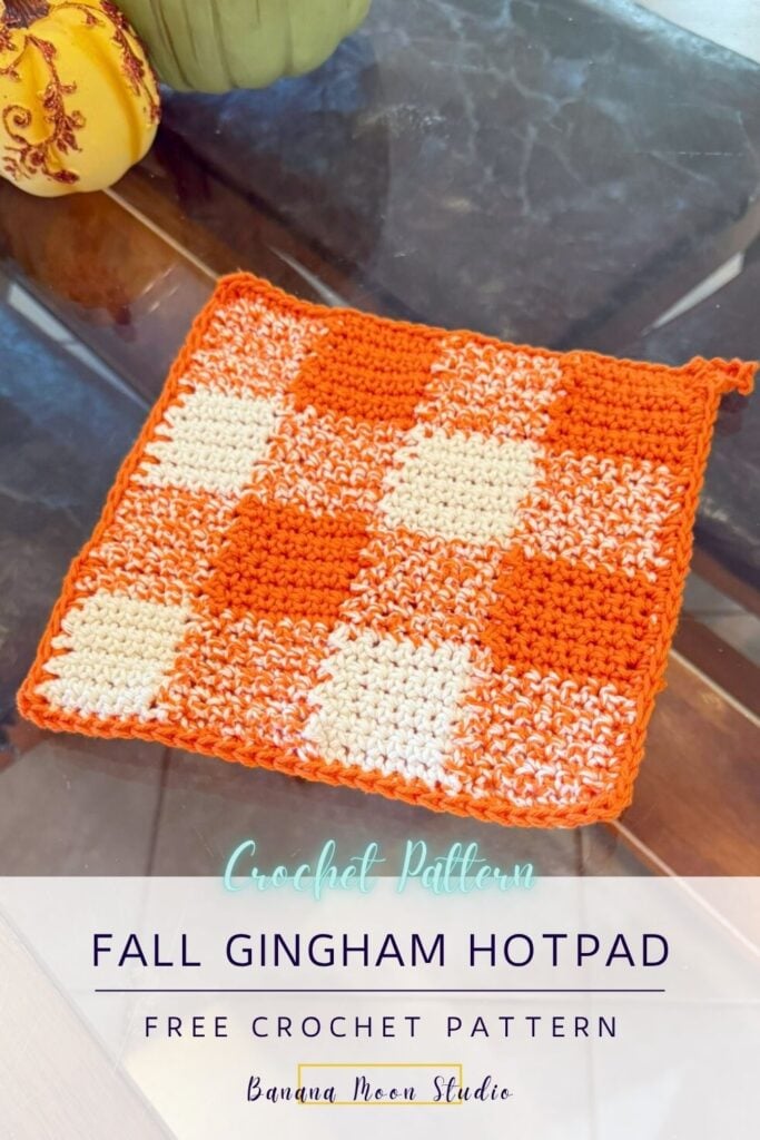 Orange and white crochet checkered pot holder on a glass table top with decorative pumpkins. a panel with text reads: Fall gingham hotpad free crochet pattern, banana moon studio.