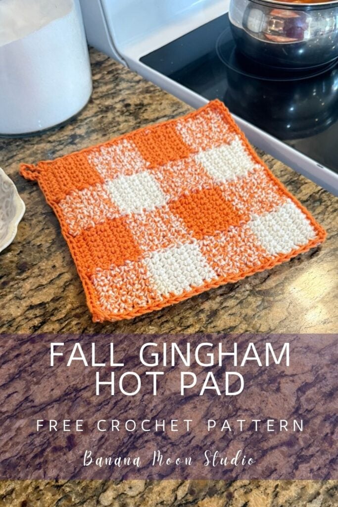 Orange and white gingham hot pad lying flat on a granite countertop. A panel with text reads: fall gingham hot pad free crochet pattern, banana moon studio.