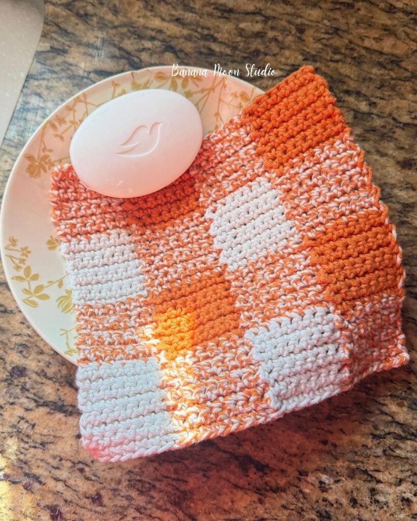 Crochet gingham dishcloth and a bar of soap in a bowl on a granite countertop. Text on the image reads: Banana Moon Studio.