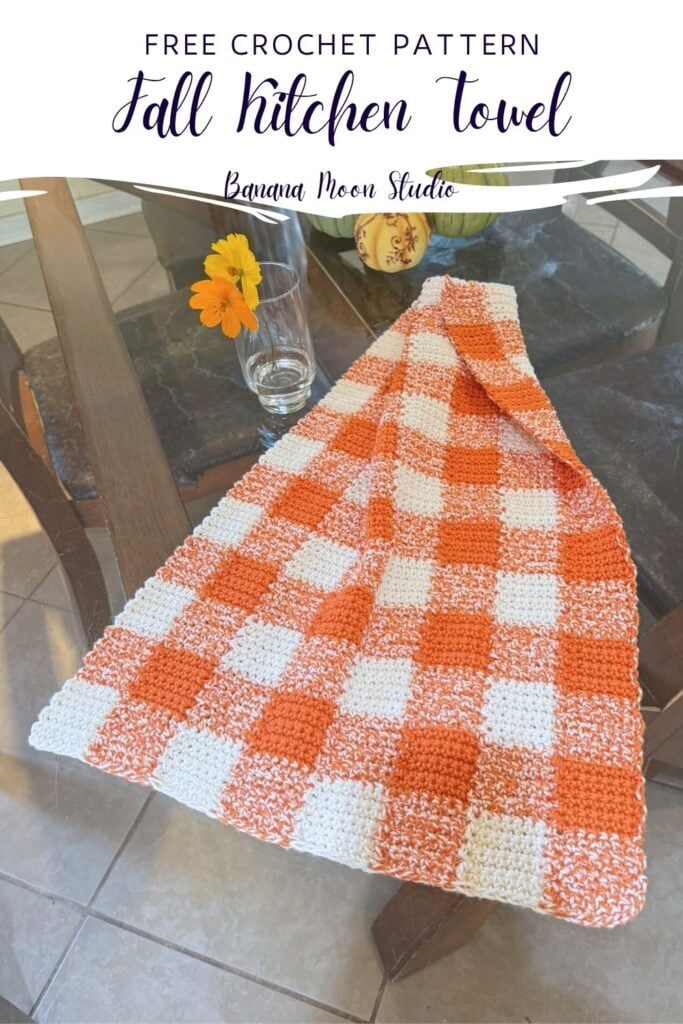 Orange and white crochet gingham kitchen towel lying on a glass table top. A panel with text reads: Free crochet pattern, fall kitchen towel, banana moon studio.