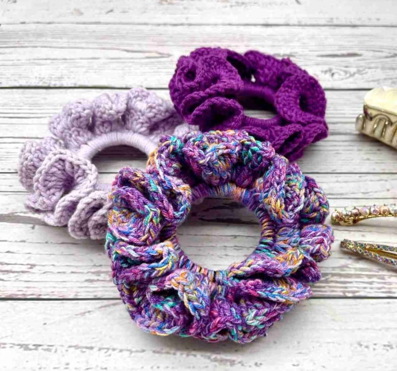 Crochet scrunchies in various shades of purple on a wooden surface.