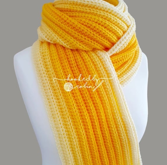 A squishy, thick ribbed crochet scarf in a yellow ombre yarn wrapped around the neck of a mannequin. 