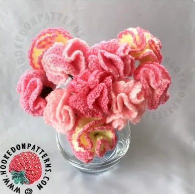 Crochet flowers that look like carnations in shades of pink and yellow in a vase. Logo and text on the image read: www.hookedonpatterns.com