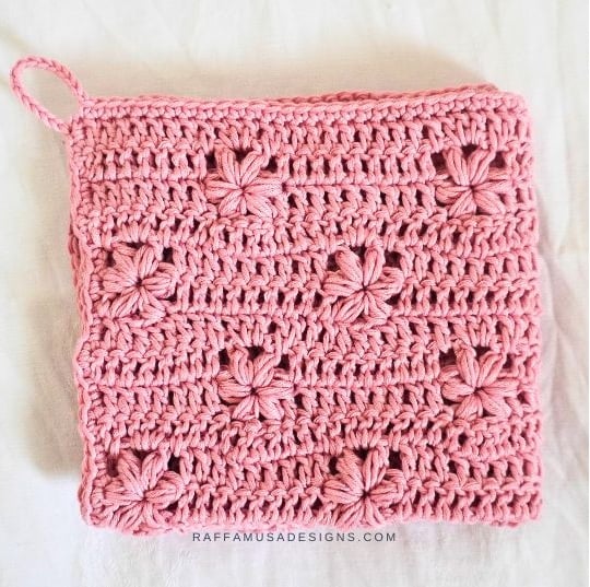 Pink crochet washcloth with flower stitches worked into the fabric. Text on the image reads: Raffamusa Designs.