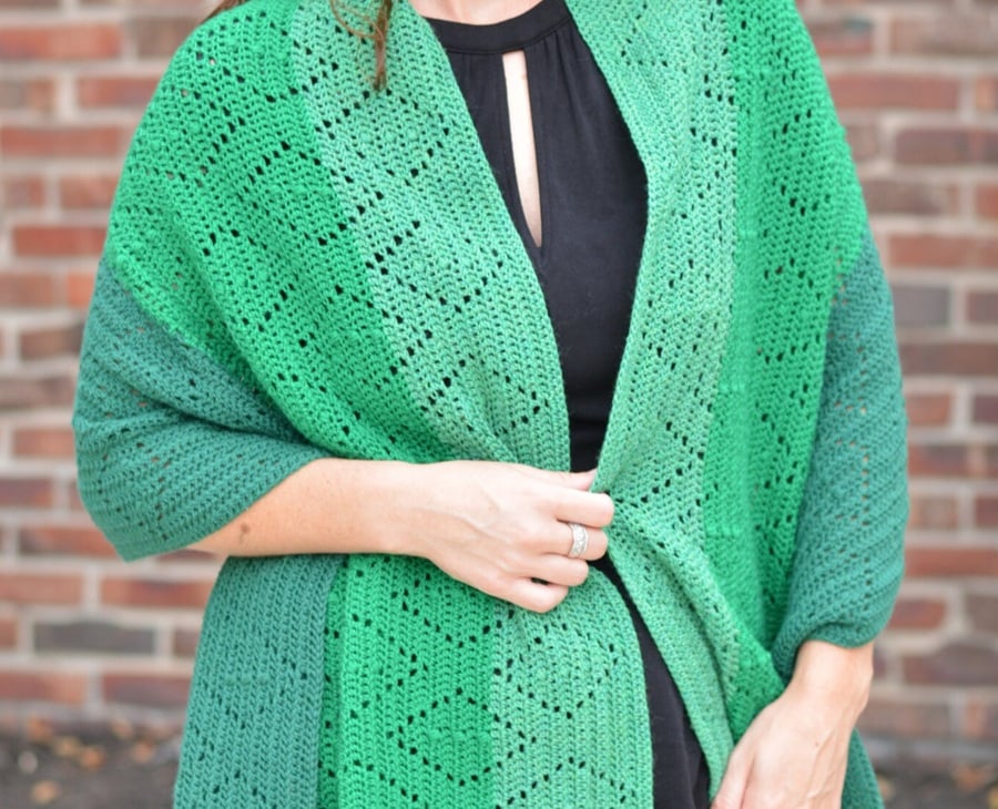 A woman wears an emerald green wrap with filet crochet diamonds on it.