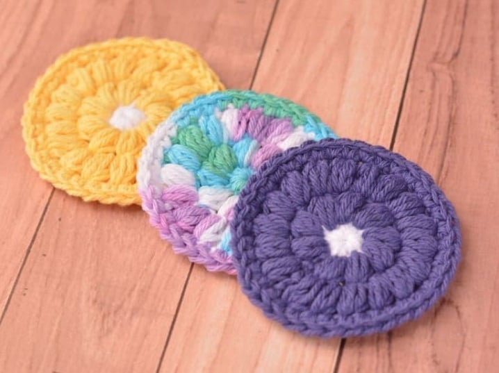 Three round crochet circles in puff stitches laying overlapping on a wooden surface.