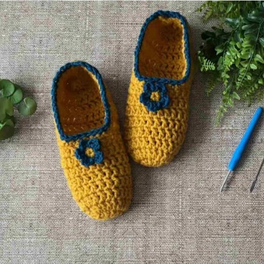 Yellow and navy crochet slippers on a woven surface with greenery.