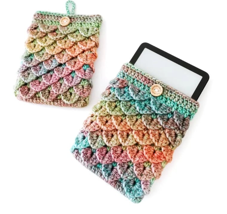 Crochet cozy with an e-reader tucked into it. It is crocheted in dragon scale stitch in a color shifting yarn.