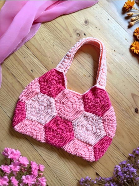 Crochet purse made of solid crochet hexagon motifs with handles added. It lies flat on a table with flowers.
