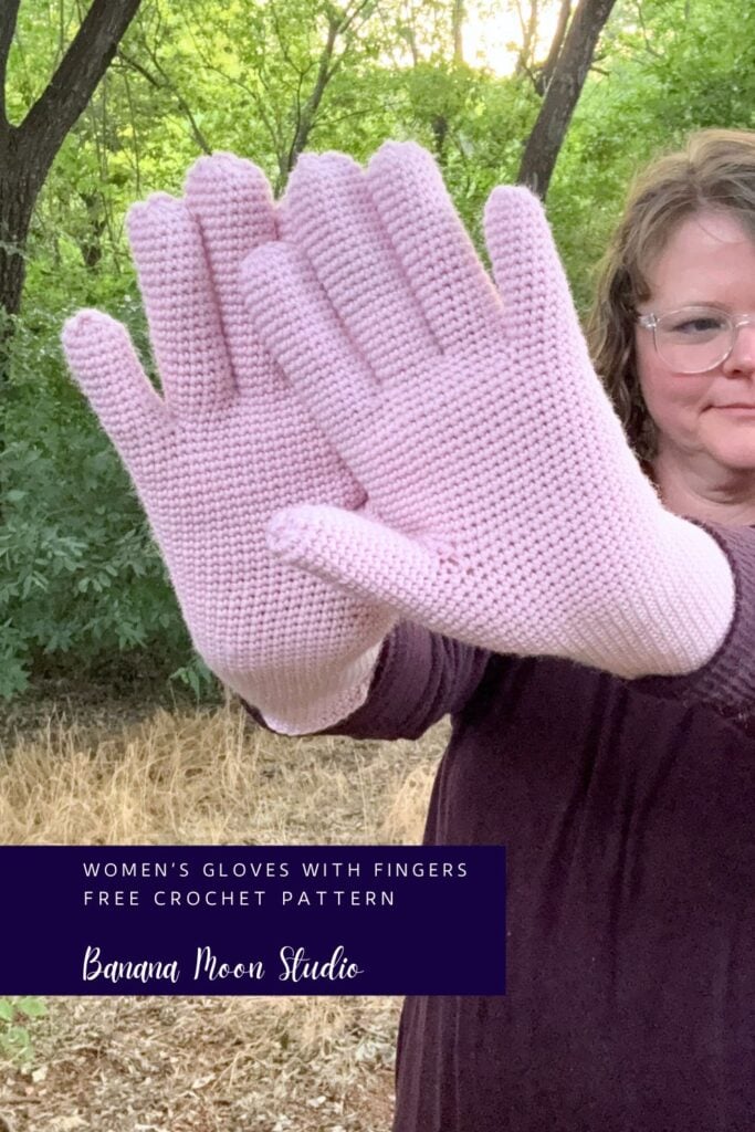 A woman standing outside holding arms out to show her pink crochet gloves with fingers. A panel with text reads: Women's gloves with fingers free crochet pattern, banana moon studio.