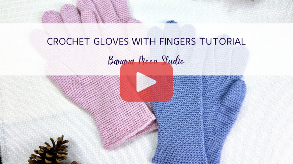 Pink and periwinkle crochet gloves lying flat on a white surface. A banner with text reads: Crochet gloves with fingers tutorial, banana moon studio. A red and white play button is centered on the image.