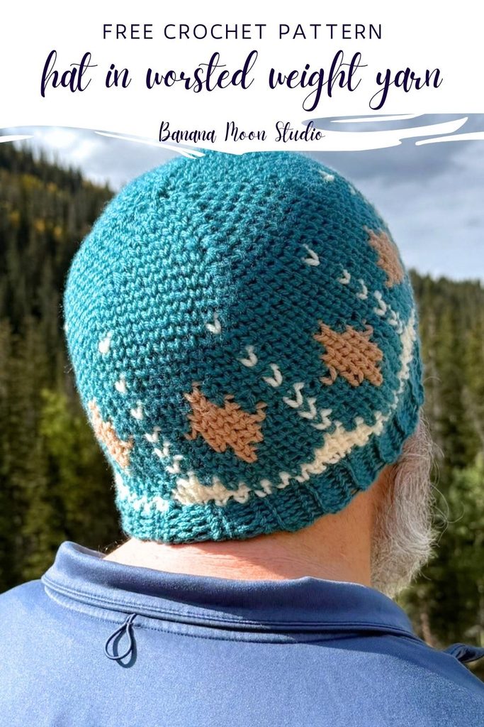 A man stands outside facing away. He wears a fair isle style crochet hat. A panel with text reads: Free crochet pattern, hat in worsted weight yarn, banana  moon studio.