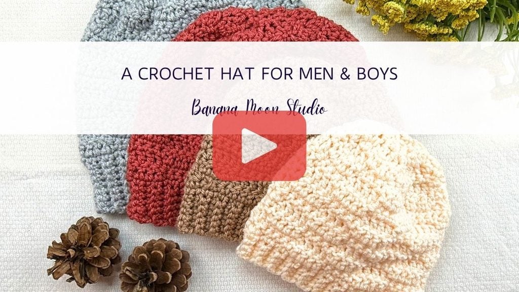 Photo of four crochet hats fanned out over a white background with pinecones and yellow flowers. A banner with text reads: A crochet hat for men and boys, banana moon studio. A red and white play icon is centered over the image.